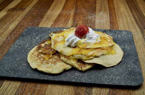 Photograph of banana pancakes topped with cream, a strawberry and syrup