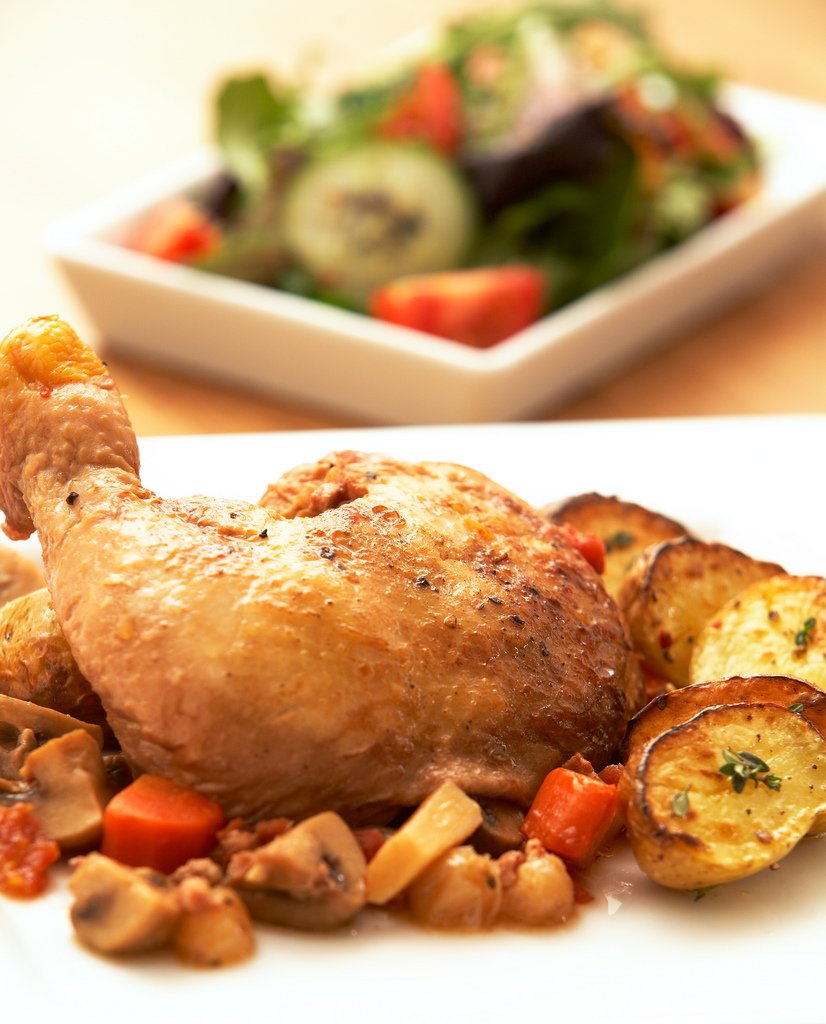Representative photograph of Coq au Vin. The photograph includes side vegetables and a different-looking wine sauce; this recipe uses red wine.