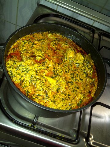 Representative photograph of Egusi Soup. The photograph shows egusi soup in a cooking pan; its meat and greens can differ from this beef-and-spinach recipe.