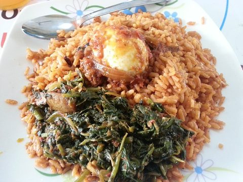 Representative photograph of Jollof Rice. The photograph includes egg and a cooked greens side; this recipe makes only the jollof rice.