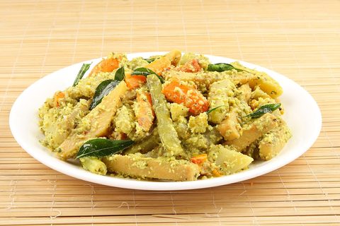 Coconut and curry leaves cover a serving of mixed vegetables; the plate underneath is white.