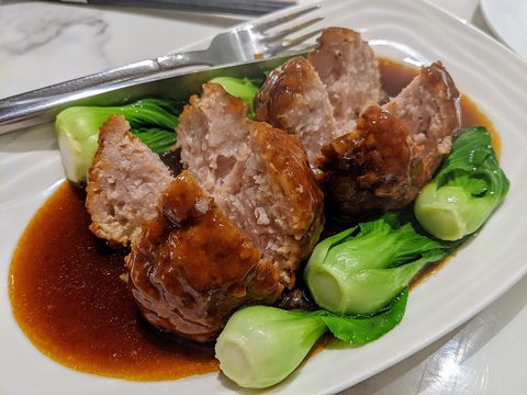 Representative photograph of Lion Head Meatballs. The photograph shows a thicker brown sauce and different greens than the cabbage broth in this recipe.
