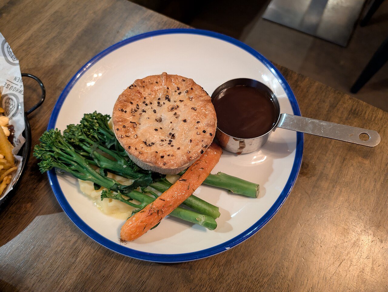 Representative photograph of Steak and Ale Pie. The photograph shows an individual pie with side vegetables; this recipe makes one large pie.