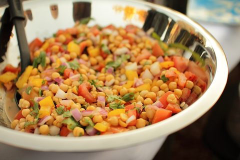 Photograph of chickpea and tomato salad with yellow pepper, red onion and herbs in a metal bowl